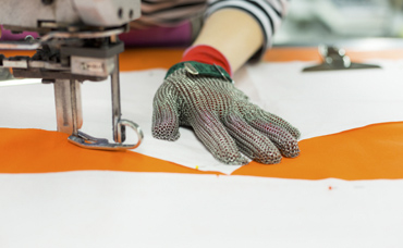Kiteen Tekstiilitehtaan ompelija ompelee ompelukoneella kangasta, kädessä on suojakäsine.
